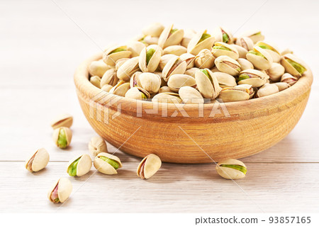 Pistachios in wooden bowl on white table, selective focus. Pistachios in wooden bowl on white table, selective focus. 93857165