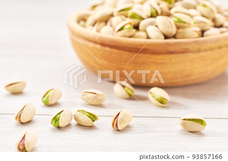pistachios spill out of a wooden bowl on a white table. pistachios spill out of a wooden bowl on a white table. 93857166