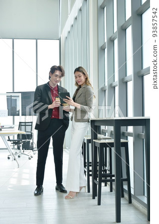 happy busimess Asian man and woman looking at mobile phone for relaxing after work in office happy busimess Asian man and woman looking at mobile phone for relaxing after work in office 93857542