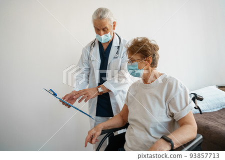 Doctor in mask explaining to a sick patient in a wheelchair the details of treatment Doctor in mask explaining to a sick patient in a wheelchair the details of treatment 93857713