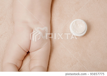 Baby is lying on a white sheets. Baby bum and feet. Mom applying some cream. Close-up of mother hands applying cream under the diaper on little baby pop. Baby is lying on a white sheets. Baby bum and feet. Mom applying some cream. Close-up of mother hands applying cream under the diaper on little baby pop. 93857775