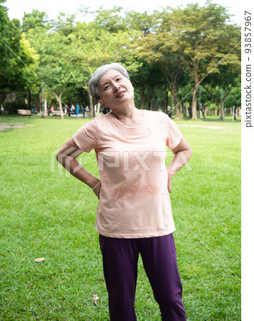 Mature Asian woman in her 60s exercising outdoors feeling uncomfortable with sore back 93857967