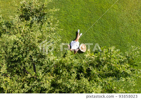 Woman in a white dress, hat with laptop, lying on the green grass under tree. Top view, drone, aerial view 93858023