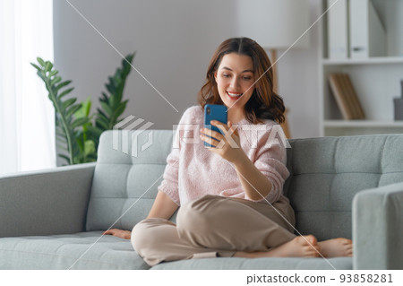 woman is using a phone sitting on a sofa woman is using a phone sitting on a sofa 93858281