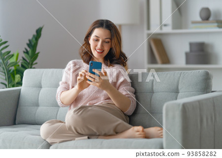 woman is using a phone sitting on a sofa woman is using a phone sitting on a sofa 93858282