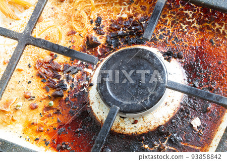 Dirty gas stove surface. Gas burner and cast iron grate of a gas oven surrounded by old leftovers of food and drinks. Top area surface and burner heads needs cleaning from burnt-on grease. Close-up Dirty gas stove surface. Gas burner and cast iron grate of a gas oven surrounded by old leftovers of food and drinks. Top area surface and burner heads needs cleaning from burnt-on grease. Close-up 93858842