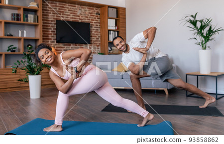 Smiling young african american male and female in sportswear doing exercises for legs or practicing yoga Smiling young african american male and female in sportswear doing exercises for legs or practicing yoga 93858862