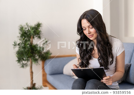 Portrait of a young woman in the office. Woman writes data to the questionnaire. 93859556