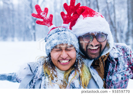 portrain of indian man and woman in red santa hat and deer horns with throwing snow on face portrain of indian man and woman in red santa hat and deer horns with throwing snow on face 93859770