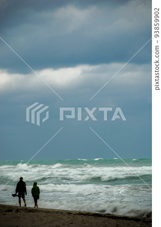 Two people walk on the beach during bad weather Two people walk on the beach during bad weather 93859902
