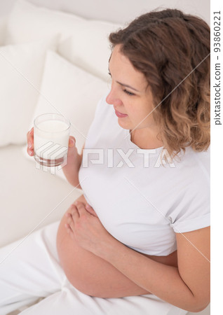A pregnant woman sits on a white sofa and drinks milk. A pregnant woman sits on a white sofa and drinks milk. 93860221