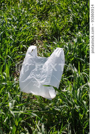 White small plastic bag lies on green grass in park or in field under sun. White small plastic bag lies on green grass in park or in field under sun. 93860914