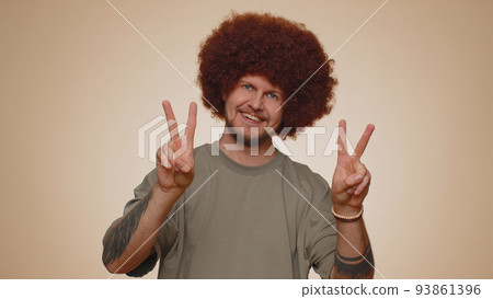 Bearded optimistic young man showing victory sign, hoping for success and win, doing peace gesture Bearded optimistic young man showing victory sign, hoping for success and win, doing peace gesture 93861396