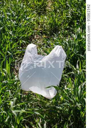 Close up on green grass lies white biodegradable bag which is alternative to regular plastic bags. 93861542
