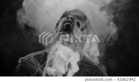 Sinister man horrible scary Halloween zombie looking ominous at camera blows smoke from nose, mouth Sinister man horrible scary Halloween zombie looking ominous at camera blows smoke from nose, mouth 93862942