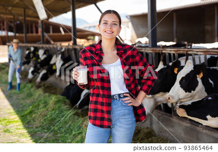 Cheerful woman is holding glass of milk at cow farm 93865464