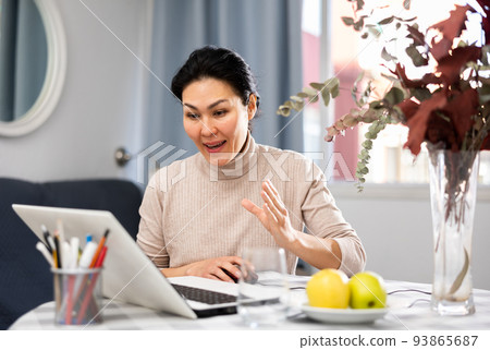Woman sitting at table at home and having video call conversation Woman sitting at table at home and having video call conversation 93865687