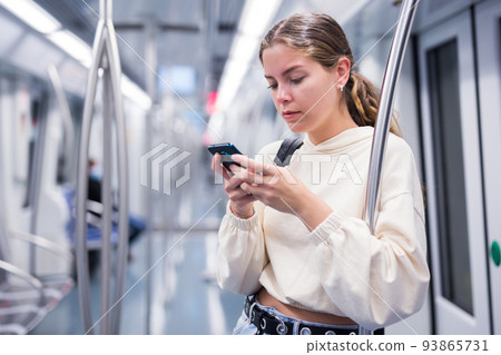 Focused girl on a subway train, texting on a mobile phone 93865731