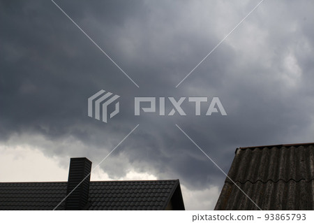 Defocus steel roof on dark sky background. Dark rain clouds above the modern roof. Roof with new black roofing tiles double flap on residential property. Dramatic sky. Out of focus 93865793