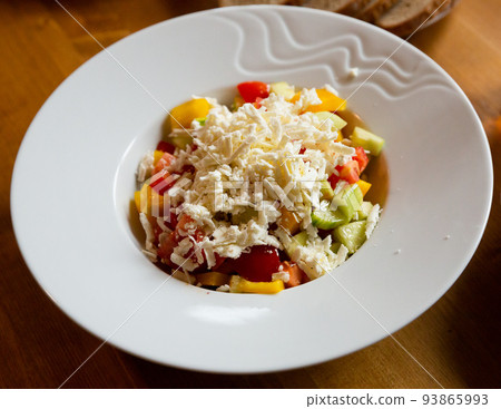 Shopska salad - dish of Balkan cuisine. Cucumbers, tomatoes, bell peppers and brynza  93865993