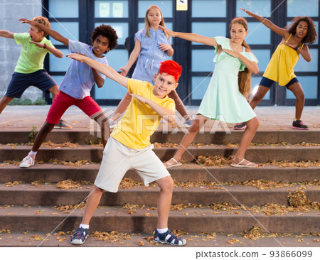 Boy dancing modern choreography with group of tweenagers on city street 93866099