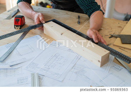 Carpenter measures wooden planks in the workshop. Carpenter measures wooden planks in the workshop. 93869363
