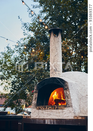 Wood-fired pizza oven with birch logs for kindling. The fire burns and the oven heats up. Vertical photo. 93869377