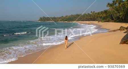 Aerial drone view of woman in swimsuit bikini relaxing and walking alone on tropical sand beach. Aerial drone view of woman in swimsuit bikini relaxing and walking alone on tropical sand beach. 93870369