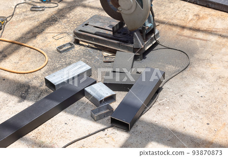 Worker cutting steel rectangular pipe in construction site. Worker cutting steel rectangular pipe in construction site. 93870873