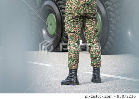 Close up of legs of soldier standing in front of metal tank. Close up of legs of soldier standing in front of metal tank. 93872230