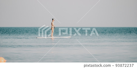 Sea woman sup. Silhouette of happy middle aged woman in rainbow bikini, surfing on SUP board, confident paddling through water surface. Idyllic sunset. Active lifestyle at sea or river. 93872237