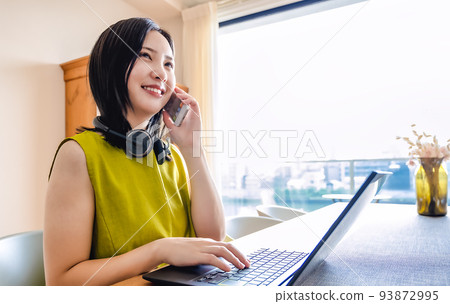 一個在家工作的年輕女人用智能手機說話 一個在家工作的年輕女人用智能手機說話 93872995