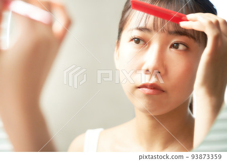 一個在鏡子前整理頭髮的年輕女子 護髮美容形象 93873359