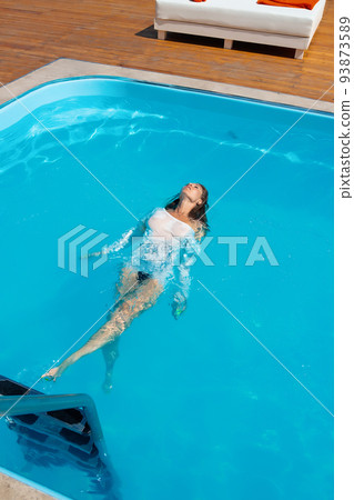 Sensual lady in wet dress standing in pool during summer vacation Sensual lady in wet dress standing in pool during summer vacation 93873589