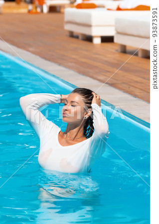 Sensual lady in wet dress standing in pool during summer vacation Sensual lady in wet dress standing in pool during summer vacation 93873591