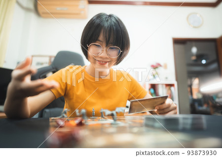 Happy young adult asian woman playing board game on top table at home eye looking camera. 93873930