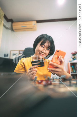 Young adult asian woman playing board game using mobile phone for shopping online for grocery. Young adult asian woman playing board game using mobile phone for shopping online for grocery. 93873961