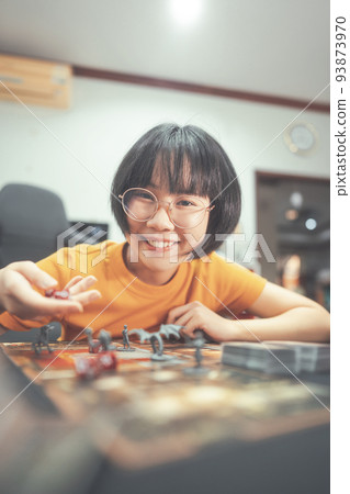 Happy young adult asian woman playing board game on top table at home eye looking camera. 93873970