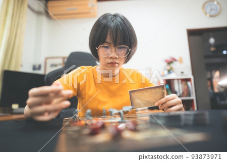 Happy young adult asian woman playing board game on top table at home eye looking camera. 93873971