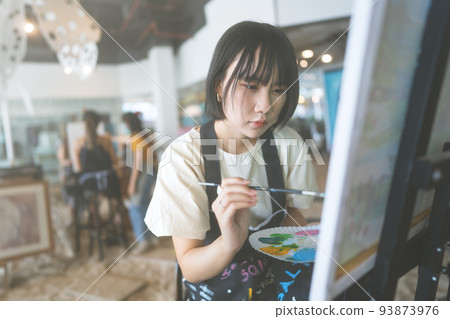 Happy young adult asian woman painting brush on canvas at workshop art lesson class. 93873976
