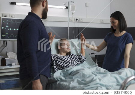 Caring parents high fiving sick little daughter under treatment resting in children healthcare facility. Loving mother and father doing high five gesture with ill girl sitting in patient bed. Caring parents high fiving sick little daughter under treatment resting in children healthcare facility. Loving mother and father doing high five gesture with ill girl sitting in patient bed. 93874060