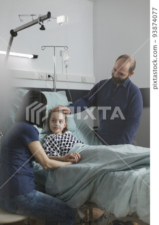 Caring parents standing beside hospitalized sick daughter inside healthcare clinic pediatric ward. Loving mother and father taking care of ill little girl resting in patient bed. Caring parents standing beside hospitalized sick daughter inside healthcare clinic pediatric ward. Loving mother and father taking care of ill little girl resting in patient bed. 93874077