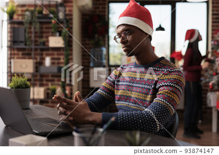 Business man working on laptop in startup office, using computer in festive workplace decorated with christmas tree and holiday ornaments. Male worker at company job during winter season. 93874147