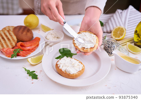 Making cream cheese and salmon toatst - woman smearing cream cheese on a grilled bun 93875340