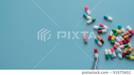 Antibiotic drug selection. Multi-colored capsule pills on blue background. Forceps picks a red-white capsule up from many antibiotic capsule pills. Chance of being selected. Probability sampling. 93875602