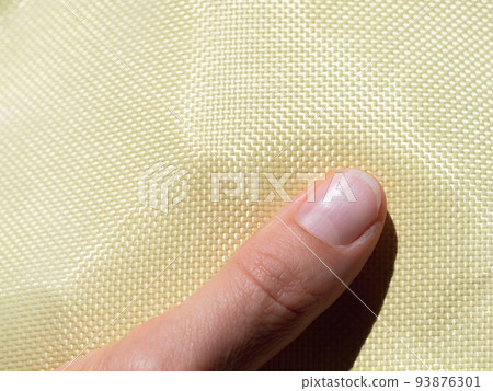Finger on bulletproof material aramid. Shining aramid kevlar background. Yellow kevlar texture and pattern. Finger on bulletproof material aramid. Shining aramid kevlar background. Yellow kevlar texture and pattern. 93876301