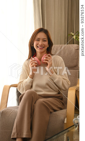 Joyful young woman listening to music on wireless headphone, resting on comfortable couch at home Joyful young woman listening to music on wireless headphone, resting on comfortable couch at home 93876534