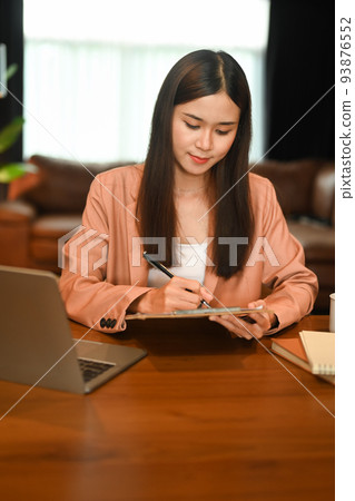 Charming asian woman sitting front of laptop and using digital tablet at her home office 93876552