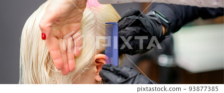 Combing hair with a comb during dyeing white hair of a young blonde woman in hairdresser salon 93877385