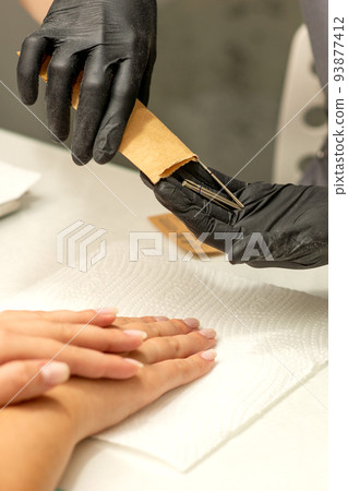 Manicure master takes out manicure tools from a kraft envelope in a nail salon Manicure master takes out manicure tools from a kraft envelope in a nail salon 93877412